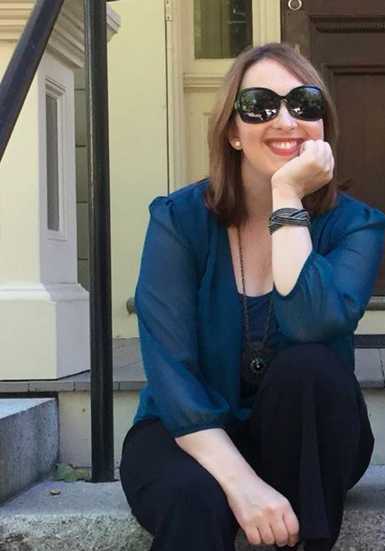 Photo of Gretchen Bostrom wearing sunglasses, a green blouse and black pants. She is sitting on stone steps.
